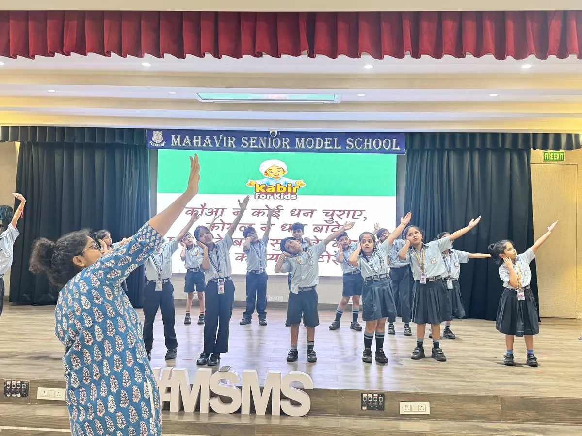 Class 2 children on the school stage for the first time, dancing to a Little Kabir Song while Shivani guides them from the front