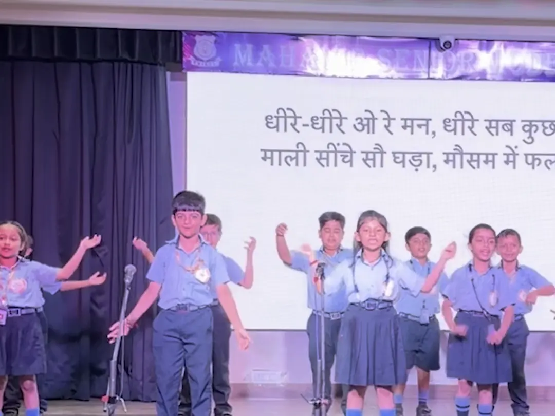 Class 2 children singing the patience song on the school stage, the words on the screen behind them
