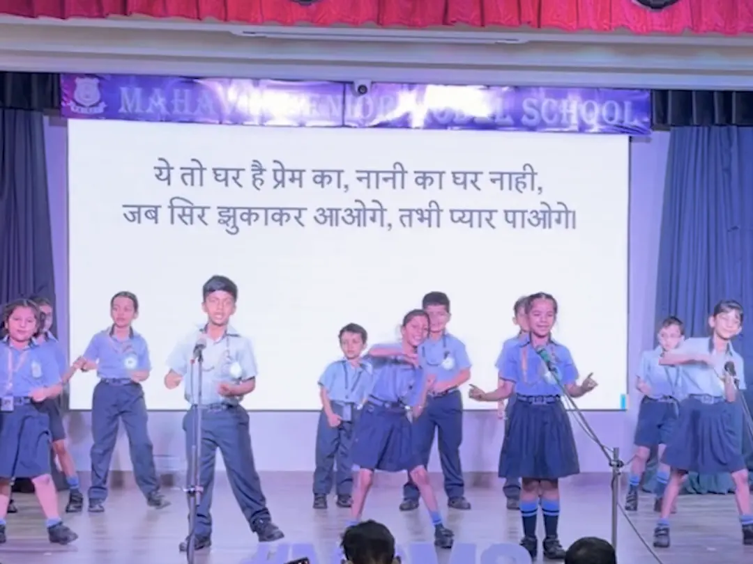 Class 2 children singing a Little Kabir Song on the school stage in front of their parents, the words on the big screen behind them