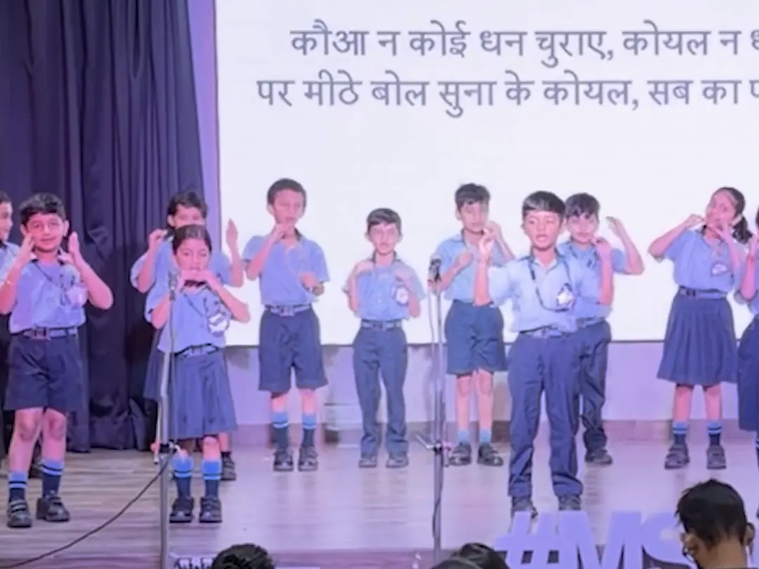 Class 2 children on stage singing the koyal song, the words on the screen
