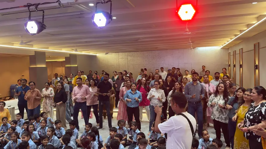 A hall full of parents on their feet with their hands up, children sitting around them