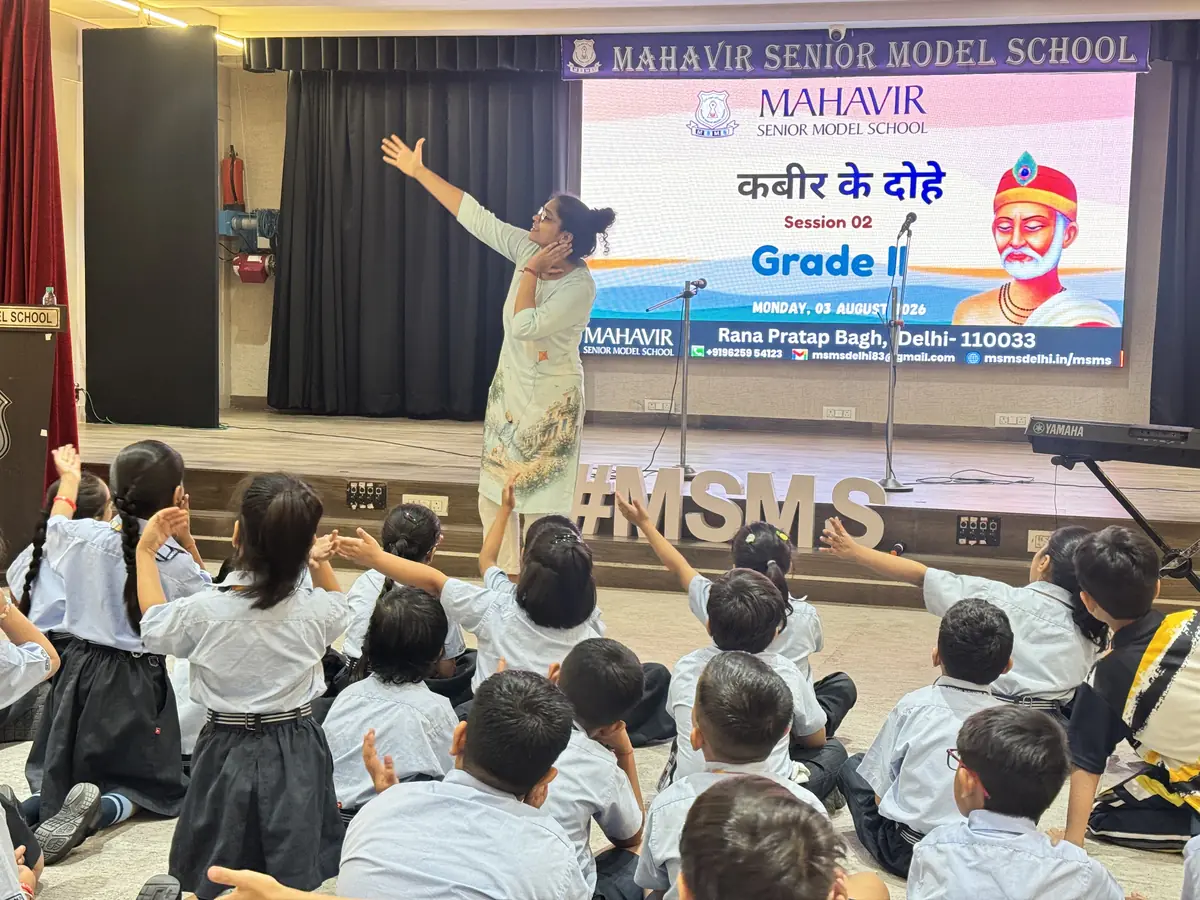 Shivani with her arm raised leading a step in Session 2 while seated children copy her